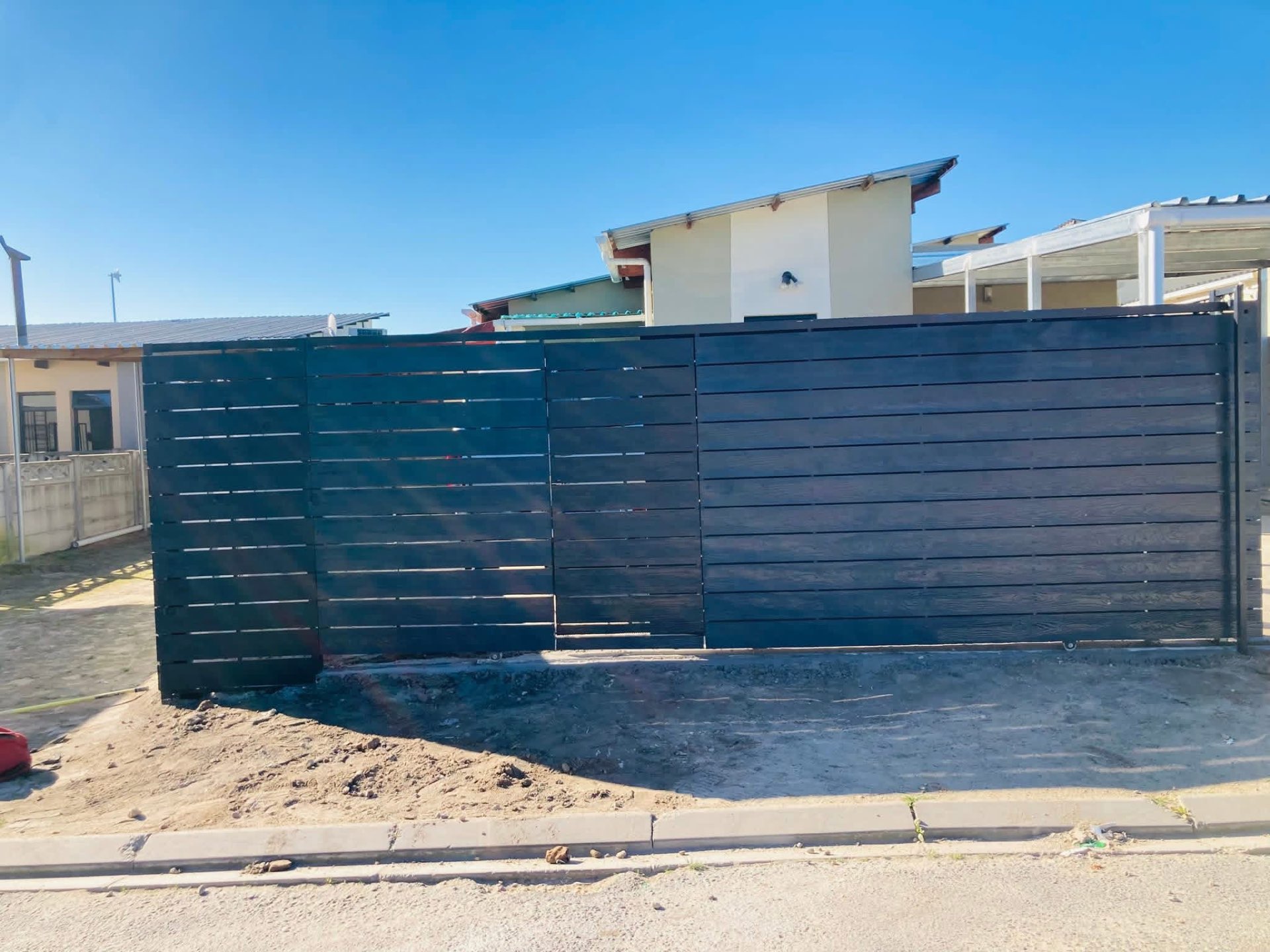 Completed dark horizontal-slat steel gates with a matching pedestrian gate at a Cape Town home