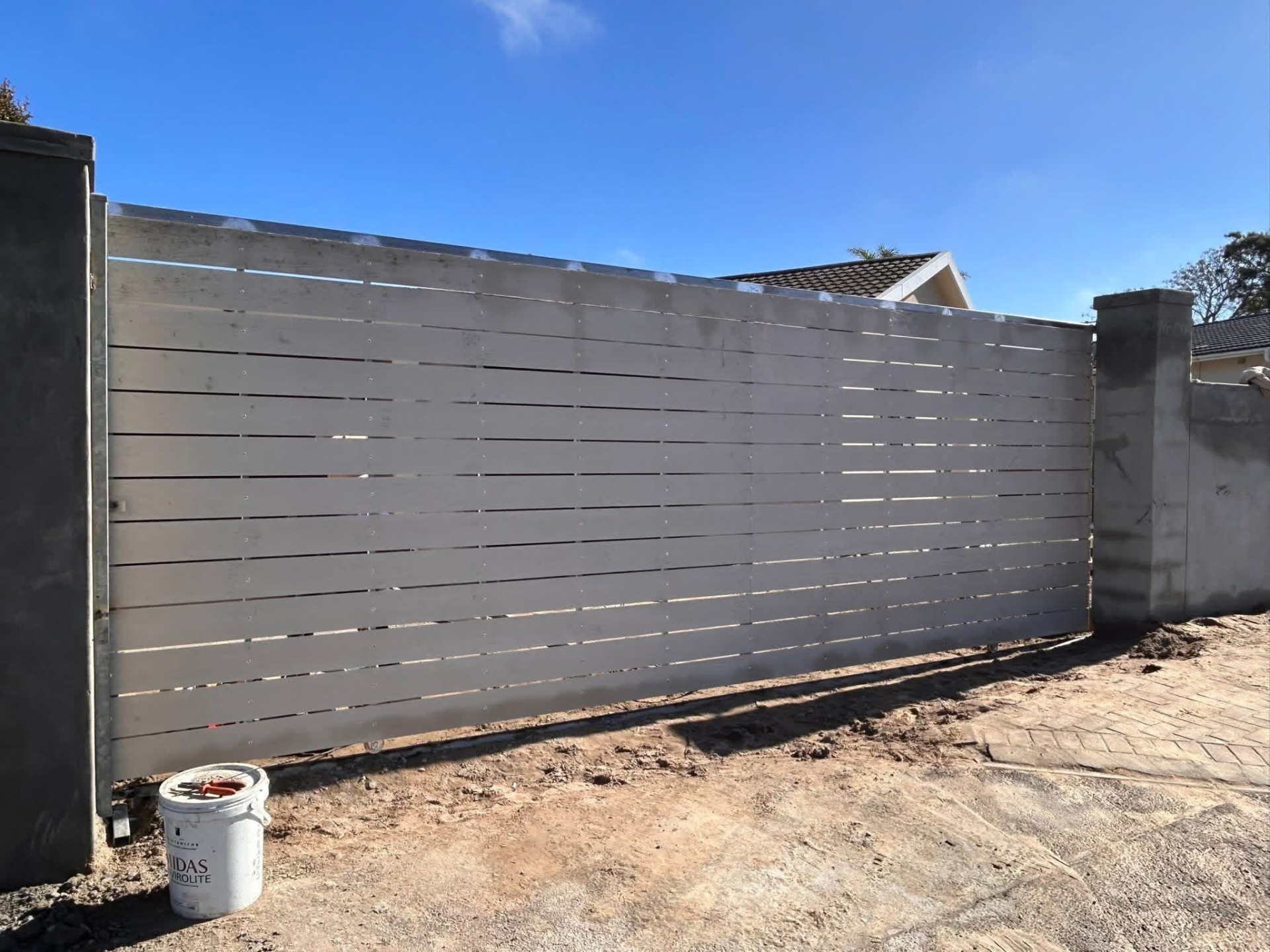 Grey primed horizontal-slat steel sliding gate fitted between plastered boundary walls