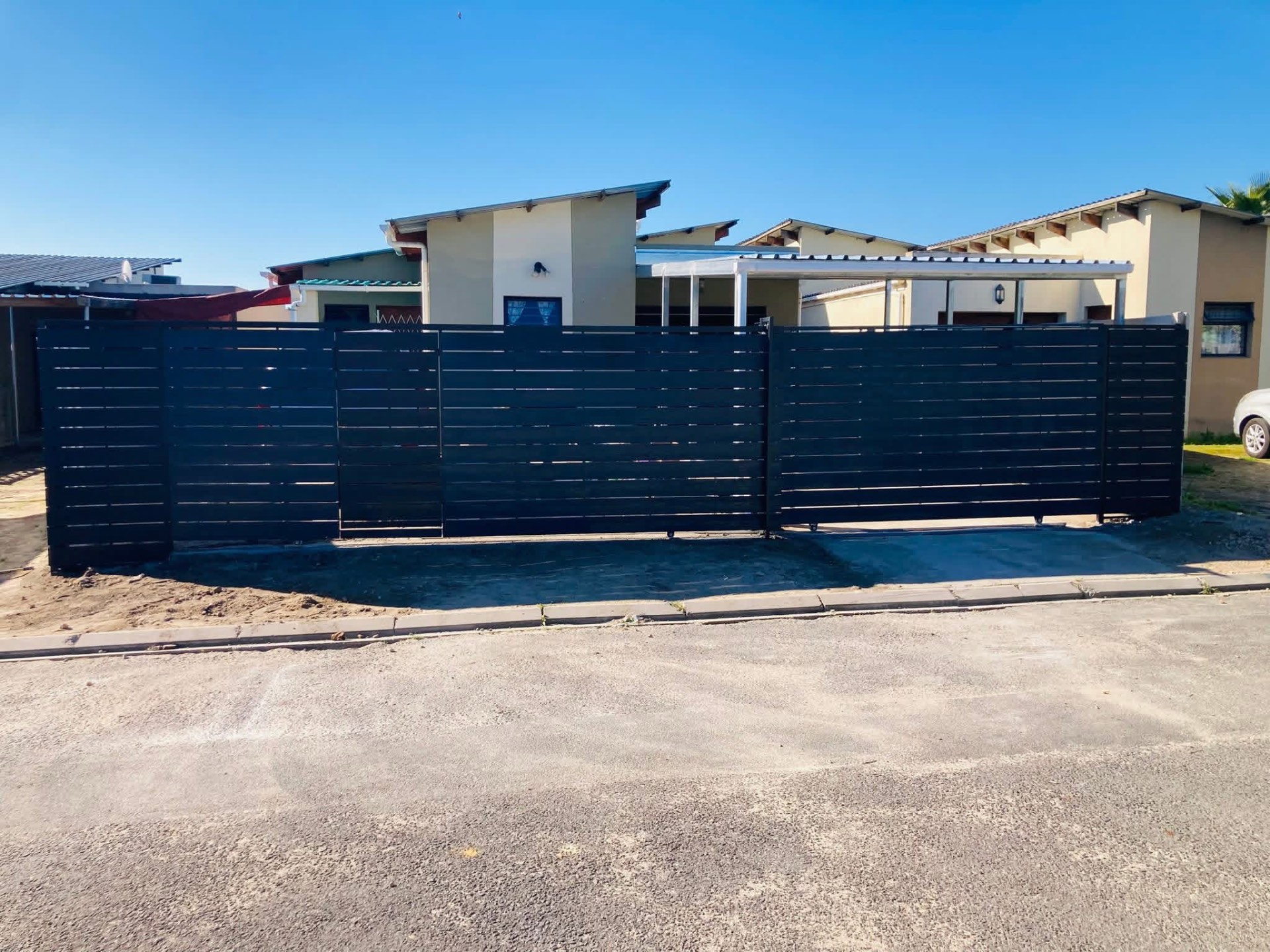 Wide black slat steel gates and boundary infill with a carport structure behind